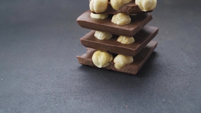 Chocolate tower with hazelnuts. Pieces of chocolate with hazelnuts on a black background. recipe for making chocolate with nuts Royalty-Free Stock Footage #1080592727
