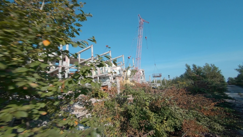 FPV drone flies quickly and maneuverable among abandoned industrial buildings and around an excavator.