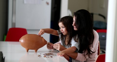 Mother and daughter financial savings adding coins inside piggy bank