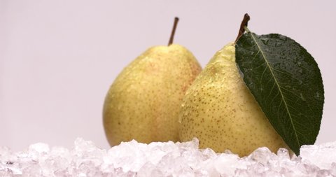 Two pears in cold ice on a white background, a drop of water drips from the pear down onto the table. Slow motion, filmed on high speed cinema camera, 4K.
