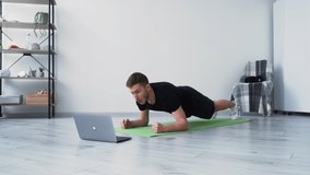 Hard training. Exhausted man. Online lesson. Lazy sport. Weak body. Stubborn guy doing plank workout with effort looking laptop in light room interior.