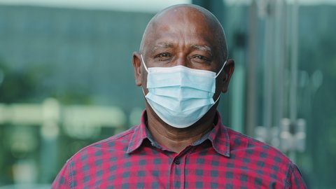 Closeup front view concerned human face portrait person wear facial mask, retired mature man pose outdoors look at camera feels afraid. COVID-19 epidemic pandemic virus outbreak protection concept