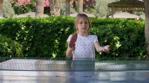 Pretty blond girl play ping pong or table tennis. Child hit lightweight ball back and forth across hard table divided by tennis net use small rackets. Sport training outdoor at summer