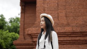 Side view of Happy traveler asian woman video call with friends via smartphone while standing at ancient temple. Smiling young girl traveling in summer trip. Travel and vacation concept.