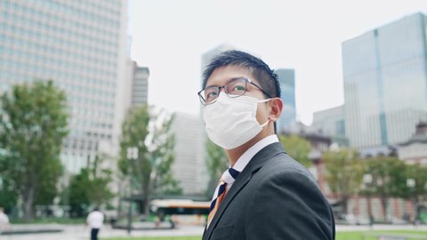 Young Asian businessman wearing a surgical mask looking up at the sky.