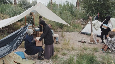 Overview shot of multi-ethnic refugees living together in tents at immigrants camp, getting food and other necessities from cardboard donation boxes sent by social workers and volunteers