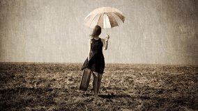 Lonely girl with suitcase and umbrella at countryside field.