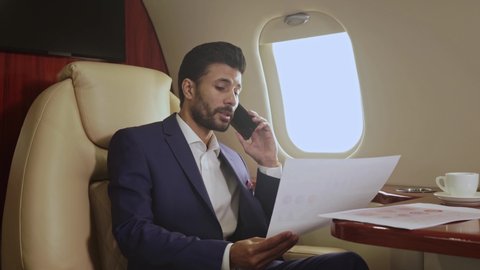 Businessman working with paper documents and talking on the phone. Flying in the private jet.