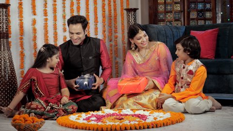 An Indian couple giving gifts to their son and daughter on the occasion of Diwali. Happy parents and their children sitting together near a floral Rangoli - Diwali decorations, a Hindu festival