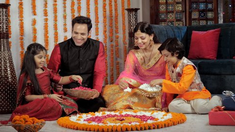 A middle-aged couple and their children decorating a Rangoli together on Diwali. Attractive parents and children enjoying Diwali holidays together - a Hindu festival, an auspicious occasion, happy.