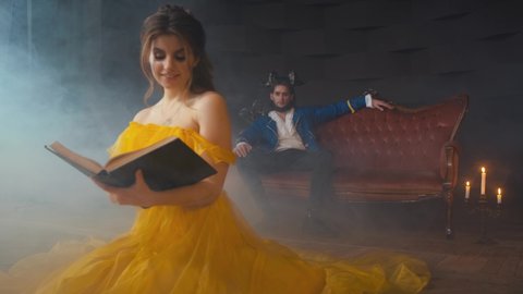 Video with noise. book without cover design. fantasy woman princess sits on floor reading. Beauty yellow long vintage dress. Enchanted prince man with horns on head. Room gothic smoke, candles burning