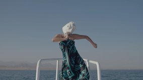 Cheerful person in unicorn head mask dancing on yacht nose. Funny dance of unicorn mask on boat in the sea. Happy vacation.