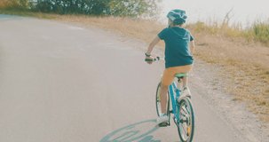 Child ride a bike. Happy cute boy in helmet learn to riding a bike in park on green meadow in summer day at sunset time. Family weekend. 4K video, Slow motion