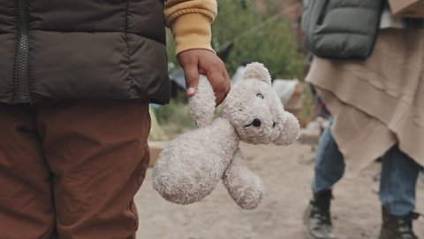Slowmo close-up of old stuffed toy in hand of unrecognizable refugee child living at tent city