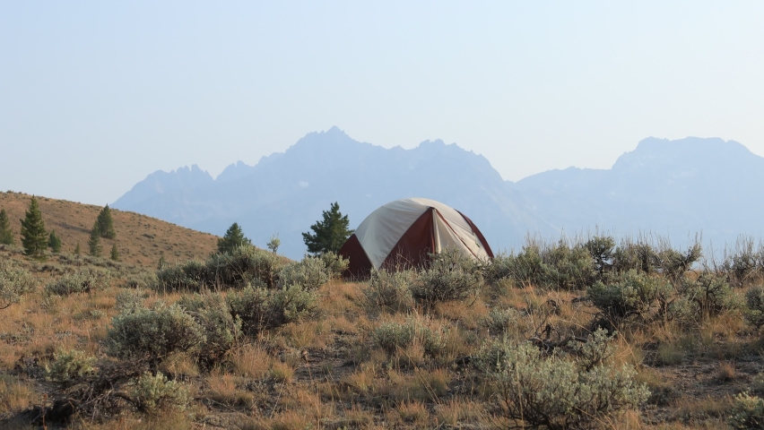 A lone camping tent is pitched amidst sagebrush near the town of Stanley in Custer County, Idaho. The Sawtooth Mountain Range and Williams Peak tower above in the distance. Summer season.