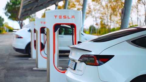 ROME, ITALY - APRIL 28, 2021: Autonomous electric Tesla car refilling battery energy on supercharger station in Rome, premium class vehicle charging battery, hybrid electric vehicle with alternative