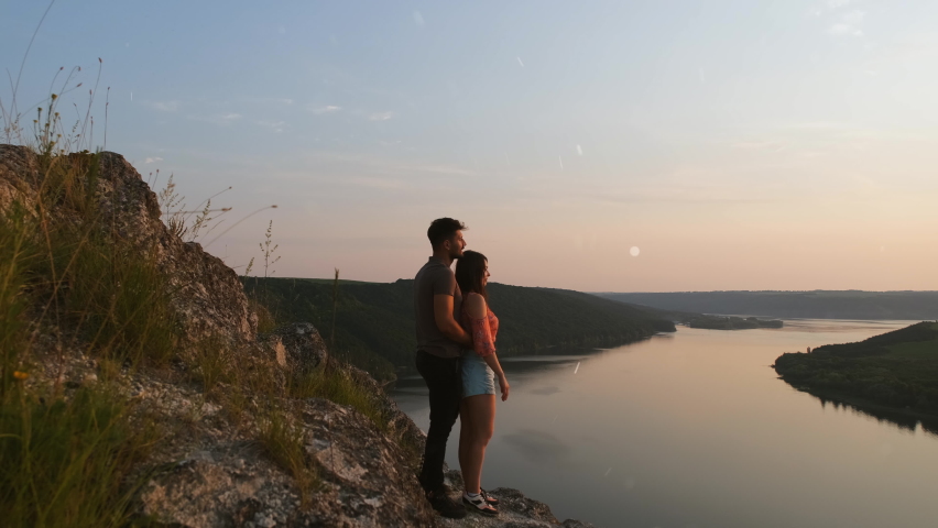 The romantic couple standing on rocky mountain top above the river. slow motion