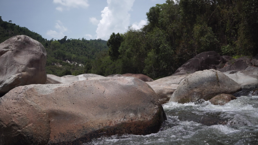 Mountain river with fast foaming clear water streams runs among huge rapids rocks against blue sky and forestry hills closeup Royalty-Free Stock Footage #1080635906