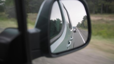 view from rear-view mirror, roadway with cars is reflected in mirror while driving around city, close-up