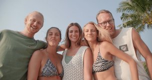 POV of young caucasian men and women hug and talk together on the beach in summer holiday with happy emotion. Group of friends smile and say hello to camera. Travel, vacation and friendship concept.