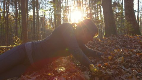 SLOW MOTION, CLOSE UP, LENS FLARE: Young woman picks herself up while tripping and falling to the leaf covered ground during her morning jog in the idyllic autumn colored forest in rural Slovenia.