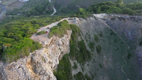 Male tourist strolls along a rocky, steep cliffside with sandy beach below. Aerial footage of the enormous, deep canyon of the harbor within the Atlantic Ocean. High quality 4k footage