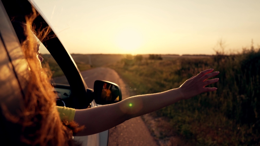 Happy girl in car window. Hair in wind. Girl travels by car. Hand in sun. Windy breeze from car window. Happy girl smiling from car window. Windy breeze in your hair. Hand in the rays of the sun | Shutterstock HD Video #1080647042