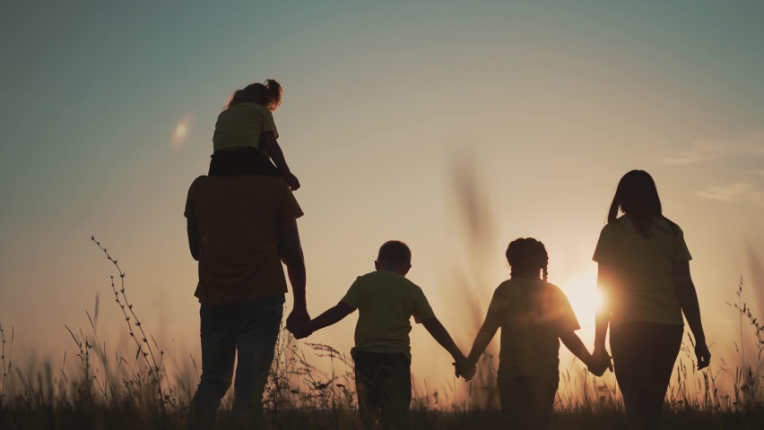 Happy family at sunset. Silhouette of group of people walk in park. Happy child with parents holding hand. Family is walk in park on grass. Happy family concept. Parents hold hand of their child. Royalty-Free Stock Footage #1080647060