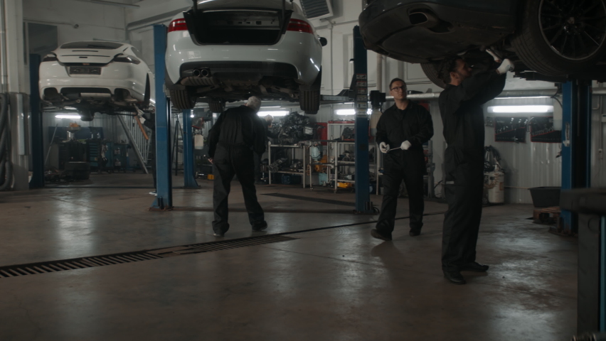 WIDE Team of mechanics wearing overalls doing some car repairs in a workshop. 50 FPS slow motion. Shot with 2x anamorphic lens Royalty-Free Stock Footage #1080647912