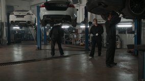 WIDE Team of mechanics wearing overalls doing some car repairs in a workshop. 50 FPS slow motion. Shot with 2x anamorphic lens - Powered by Shutterstock - Get 15% off with code: PIKWIZARD15