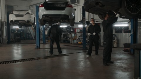 WIDE Team of mechanics wearing overalls doing some car repairs in a workshop. 50 FPS slow motion. Shot with 2x anamorphic lens