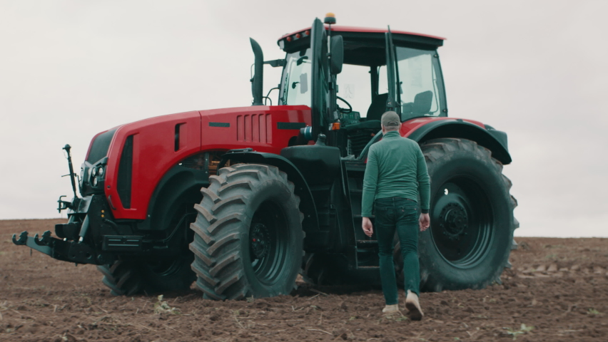 Hero shot portrait of 50s farmer walking towards tractor early in the morning in the field. Shot with 2x anamorphic lens Royalty-Free Stock Footage #1080647939