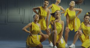 4k Group of beautiful , funny, stylish girls in yellow dresses dancing inside pavilion with grey background  . Synchronized dance of female ensemble for video clip  Woman dancers with the same outfit 