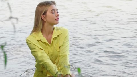  Beautiful blond romantic woman enjoying summer vacation at summer beach. Portrait of gorgeous girl in yellow outfit relaxing by water. Summer outdoor pleasure 4K