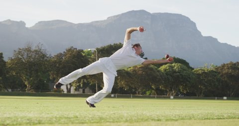 Front view of a Caucasian male cricket player wearing whites, standing on a cricket pitch, diving for the ball and failing to catch it during a match on a sunny day, in slow motion