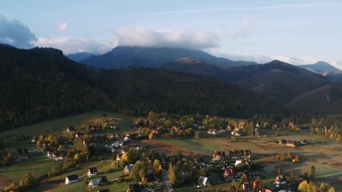Aerial view flight over mountain village lit with warm sunlight. Drone shot beautiful highland valley in sunset light. Picturesque Tatras mountains range covered with clouds, Poland, Zakopane