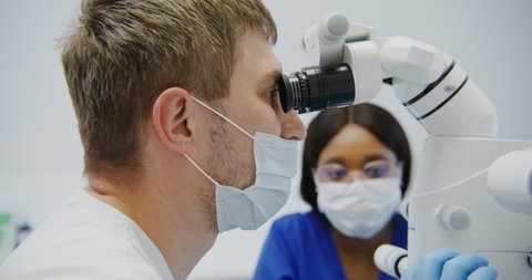 A male dentist of European appearance looks through a dental microscope for the treatment of a patient's tooth root canal. Removal of a nerve in a tooth with a modern method.