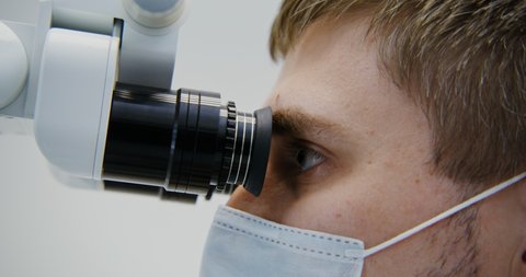 A male dentist of European appearance looks through a dental microscope for the treatment of a patient's tooth root canal. Removal of a nerve in a tooth with a modern method, close-up