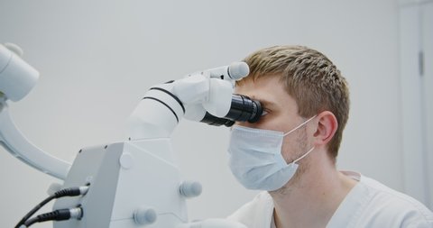 A male dentist of European appearance looks through a dental microscope for the treatment of a patient's tooth root canal. Removal of a nerve in a tooth with a modern method, close-up