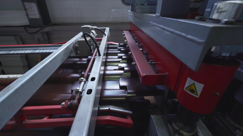 Brown metal roof tiles made from galvanized and painted steel in metal sheet forming machine in metalwork factory