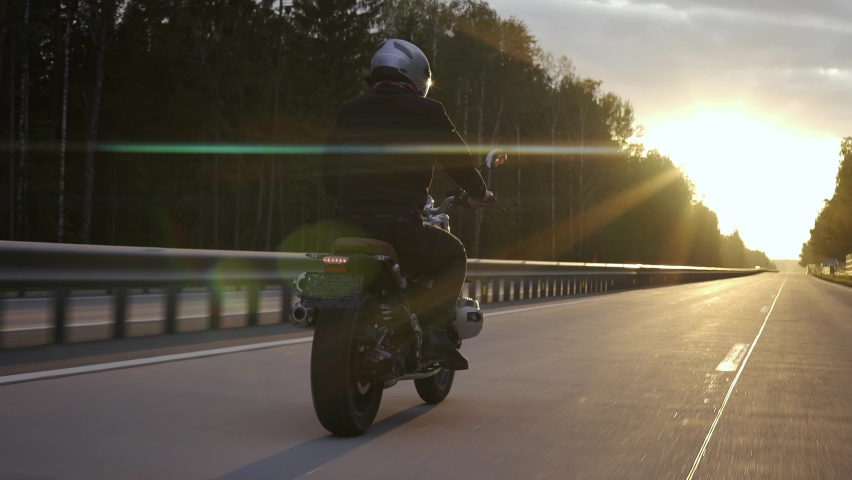 Man riding scrambler motorbike on the highway through the forrest at the sunset. Man riding cafe racer on the highway, back view. High quality 4k footage | Shutterstock HD Video #1080661127