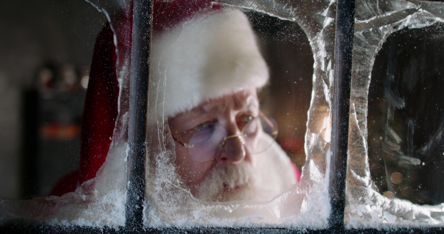 Santa Claus looking out window close-up, staring outside, taking bag full of presents for children. Christmas and New Year concept. Happy holidays and winter traditions. 