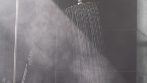 Running hot water streams make vapor in sunlight ray in grey tiled bath cabin equipped with deluxe thermostatic shower system