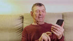 Elderly man dials number and speaks in smartphone from home. Old senior talking on video call in mobile phone . High quality 4k footage
