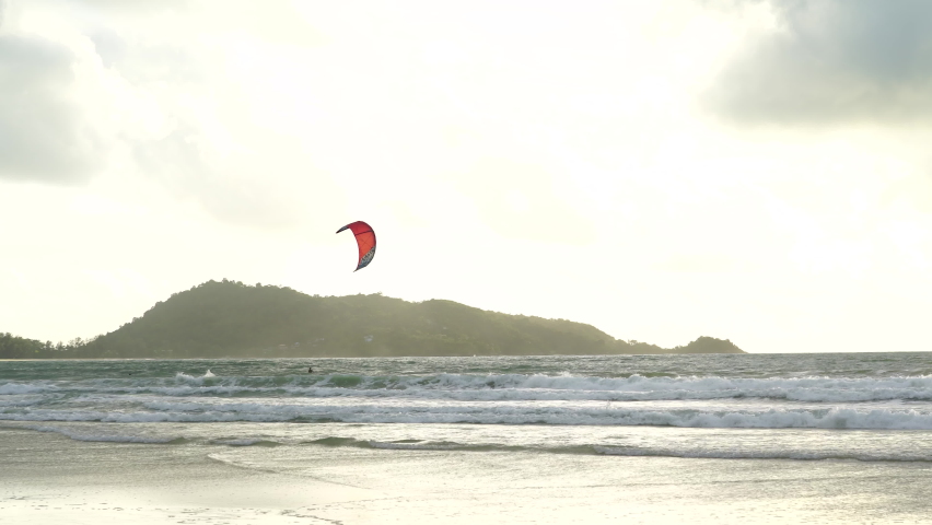 Tourists Kite-surfing race slow motion flying on sky during sunset mountain background.Sailboard beach relax weekends.Kite surfing race over sea summer vacation and holiday.Video 4K