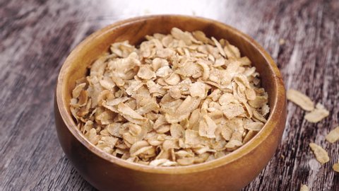 A full wooden bowl of dry cereal wheat spelt flakes. Rotation. Close up. On a wood table
