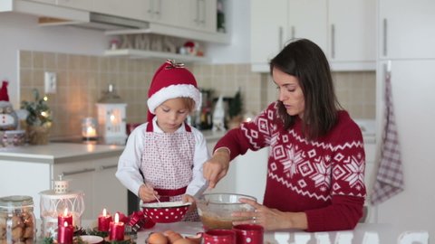 Cute blond child, boy and his mom, baking christmas cookies at home, having fun