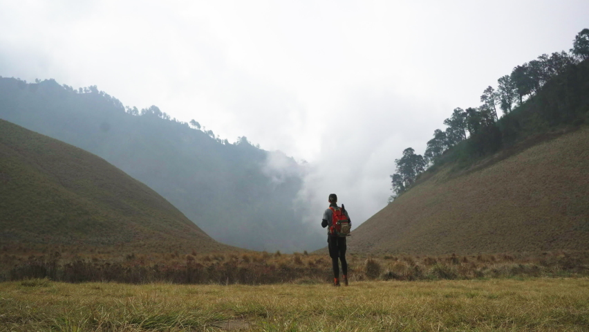 Tourist man with large red backpack looks at picturesque hills with forest and mist standing in empty field backside view Royalty-Free Stock Footage #1080672098