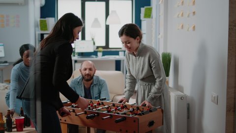 Colleagues playing foosball game and woman winning, having fun with football table after work. Workmates enjoying drinks at office, having bottles of beer and pizza to celebrate party
