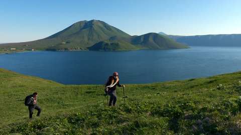 Couple tourists walking on krenitsyn volcano on the Kuril islands, watching the sunrise, hiking tourism, mountains at sunrise. Concept of nature and wildlife of Japan and kuril ridge